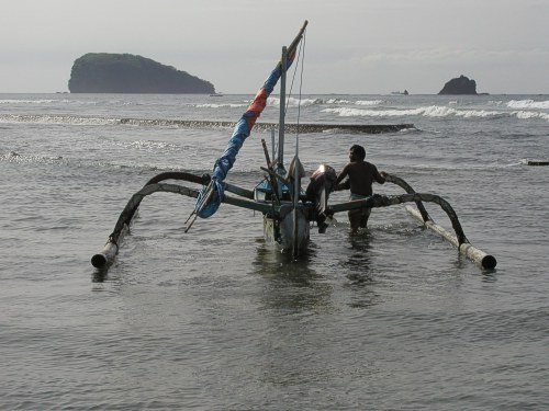 Ein Fischer schiebt sein Boot ins Meer